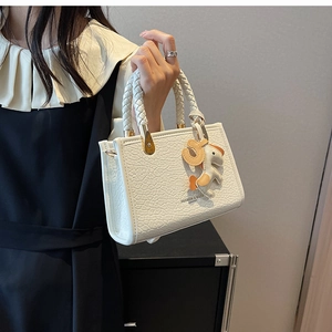 Close-up of white crocodile embossed leather tote with woven handle and animal charm