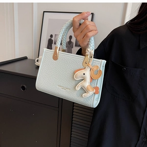 Close-up of light blue textured leather tote bag with braided handle and pony charm