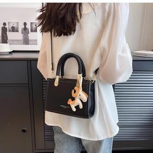 Detail of black crocodile texture tote bag with woven handle and horse charm on shoulder
