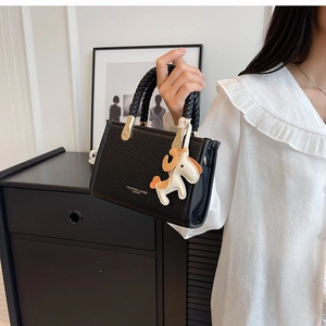 Detail of black crocodile embossed tote bag with braided handle and pony charm accent