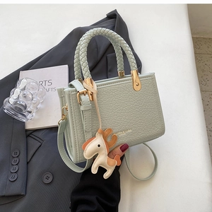 Close-up of mint green croc-embossed mini tote bag with woven handle and horse charm