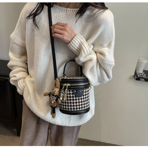Detail of houndstooth cylinder crossbody bag with rabbit charm shown on a model