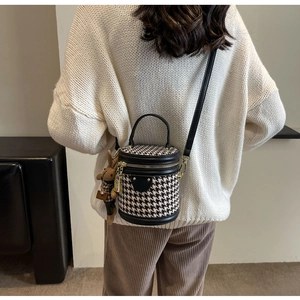 Detail of houndstooth cylinder crossbody bag with plush rabbit charm on a model