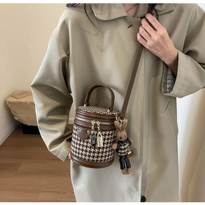 Chic vintage houndstooth bucket bag with rabbit charm worn as a stylish crossbody bag.