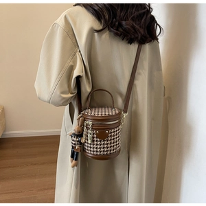 Detail of houndstooth crossbody bucket bag with bear charm and brown leather handle