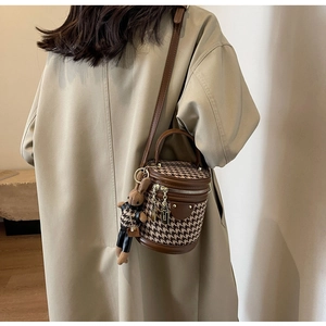 Detail of houndstooth cylinder crossbody bag with cute bunny pendant on khaki coat