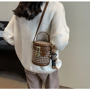 Detail of houndstooth bucket bag with rabbit charm worn by model in cream knit sweater