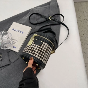 Close-up of houndstooth bucket bag with gold zipper and leather trim on grey blazer