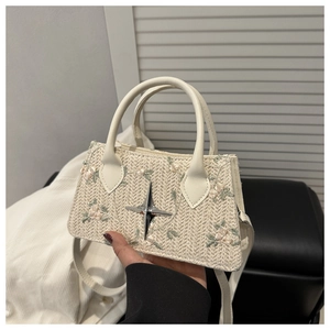 Dettaglio borsa di paglia con ricamo floreale e accessorio a stella metallica