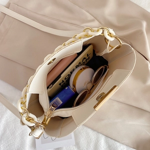 Sac seau beige à chaîne avec grande capacité et accessoires du quotidien sur fond en tissu