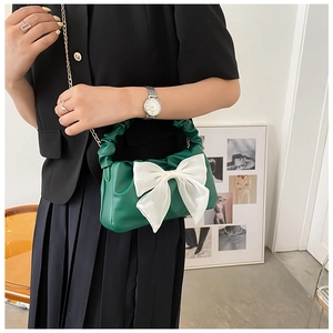Detail of dark green pleated handbag with large white bow and gold chain strap