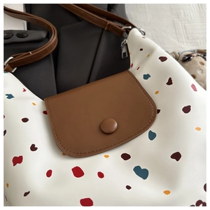 Dettaglio di una borsa bianca a pois colorati con tracolla in pelle e ciondolo in peluche