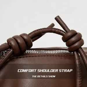 Detail showing brown leather crossbody bag with knotted shoulder strap and zipper closure