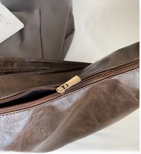 Detailed close-up of smooth gold metal zipper on dark brown textured faux leather bag