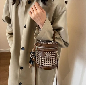 Houndstooth barrel bag with brown leather trim and bear charm on a beige coat model