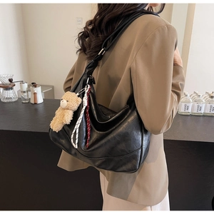 Detail of minimalist black PU leather hobo bag with cute plush bear and braided charm