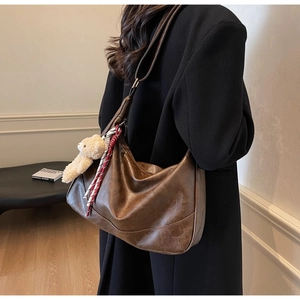 Detail of soft brown PU leather hobo bag with teddy charm on a black coat