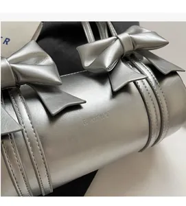 Detail view of silver ballet-style cylinder bag with leather bow and embossed text