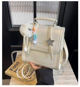 Close-up of off-white crossbody bag with metal star studs and a plush charm on a book