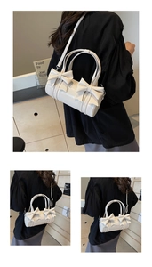 Close-up of a white cylindrical crossbody bag with elegant bow details and dual ring handles