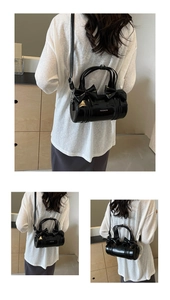 Detail of black patent leather cylinder bag featuring large decorative bows and handles