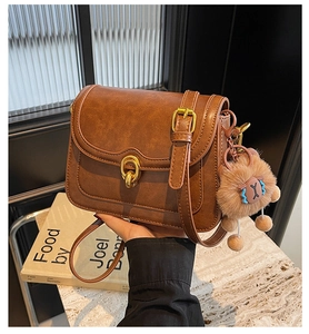 Detailed close-up of brown vintage crossbody bag with gold hardware and plush charm