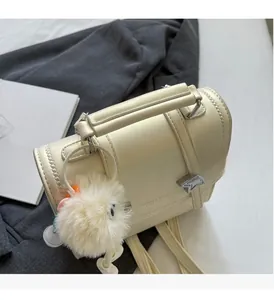Detail of cream beige PU leather crossbody bag with plush charm on a grey blazer background