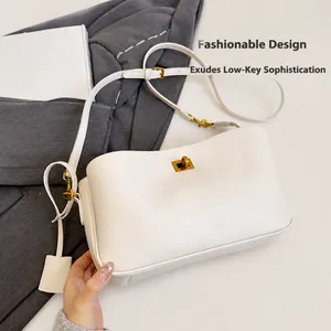 Detail view of a white leather handbag with a polished gold twist lock and a matching strap