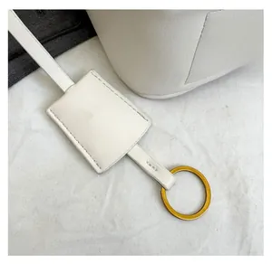 Close-up of white leather key fob detail with gold ring and precision stitching on handbag