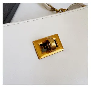 Close-up of golden turn-lock hardware and fine stitching on a white leather shoulder bag