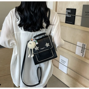 Detail of black leather crossbody bag with silver star and plush doll charm on a model