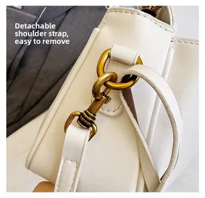 Close-up of detachable shoulder strap with matte gold metal clasp on white leather bag