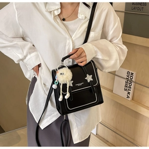Detail of black leather crossbody bag with silver stars and a white plush eye charm