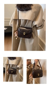 Detail of dark brown vintage crossbody bag with gold buckle and a bear plush charm