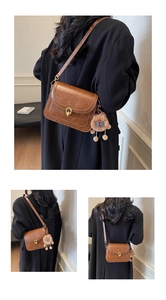 Brown vintage leather crossbody bag with golden turn-lock and plush lion pendant detail