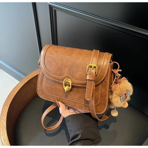 Detail view of brown textured leather crossbody bag with golden lock and lion charm