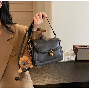 Detail of matte black leather handbag with a vintage gold knot buckle and plush lion charm