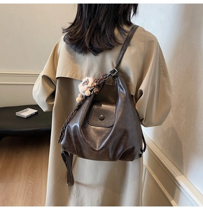 Brown pleated tote bag detail on model featuring button flap and plush charm