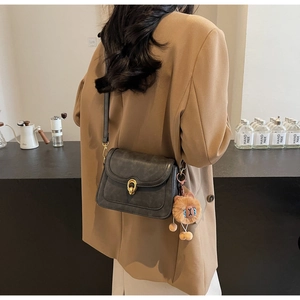 Detail of grey crossbody bag with golden buckle and plush lion charm worn with brown blazer