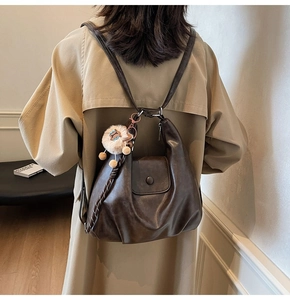 Detail of dark brown leather backpack with minimalist flap and cute lamb charm accessory
