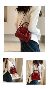 Detail view of burgundy patent leather handbag with top handles and shoulder strap