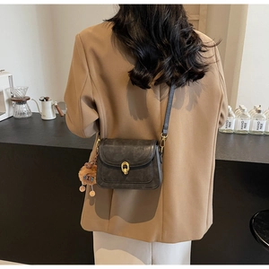 Detail of dark grey retro crossbody bag with gold U-buckle on a camel blazer