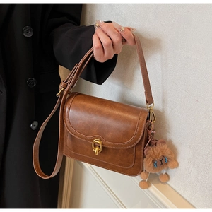 Close-up of vintage brown PU leather crossbody bag featuring gold ring buckle and bear charm