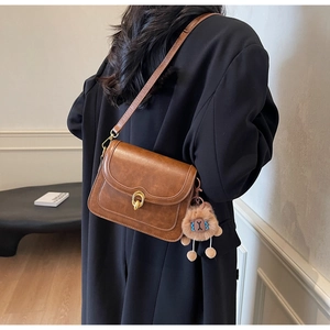 Detail of vintage brown crossbody bag featuring a golden ring lock and plush lion charm