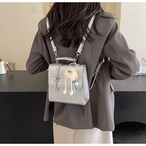 Close-up of silver PU leather backpack with star charm and plush pompom accessory