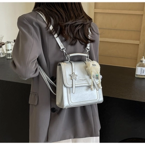 Silver metallic backpack with star accents and white plush charm on model