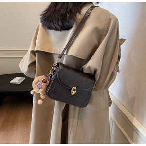 Detail of dark brown vintage crossbody bag with a cute sheep charm on a tan trench coat