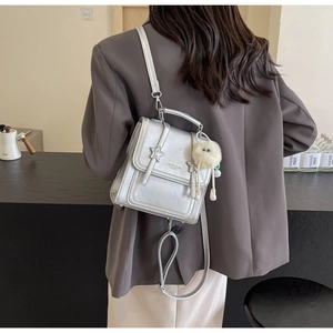 Silver metallic PU backpack with star stitching and plush ball charm shown on a model