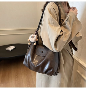 Detail of dark brown leather hobo bag with vintage texture and cute lion plush pendant