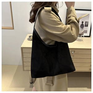 Dettaglio di una borsa tote nera con tracolla larga indossata su un trench color cammello